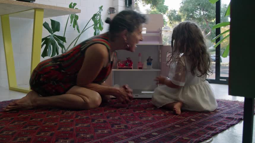 Grandmother and granddaughter rub noses together as they play with a dollhouse