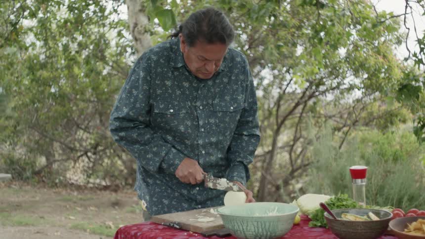 A man stands outside and cuts an onion as he prepares food