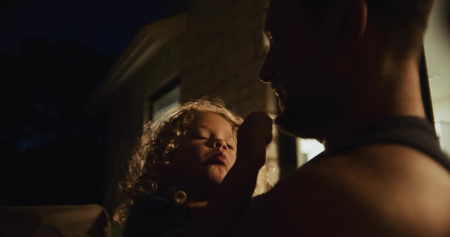 A child sitting on dads lap plays with his chin hair and makes faces
