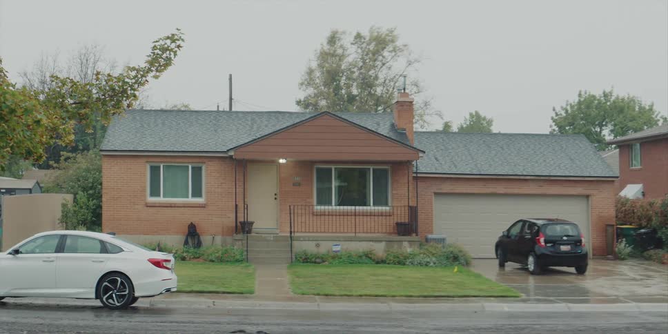 Rain falling on a typical neighborhood home with a car parked in the driveway