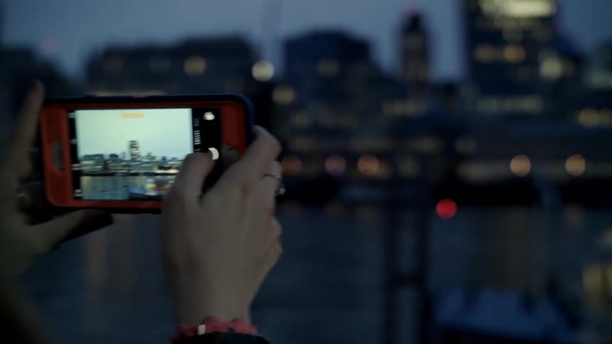 A woman focuses in to take a picture of a skyline on her cellphone