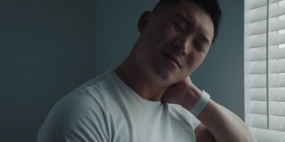 A man grimaces as he stretches his stiff and sore neck