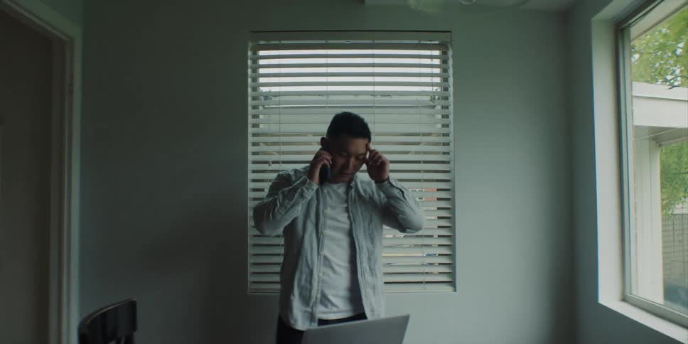 A man looks very worried as he looks at a laptop and talks on the phone