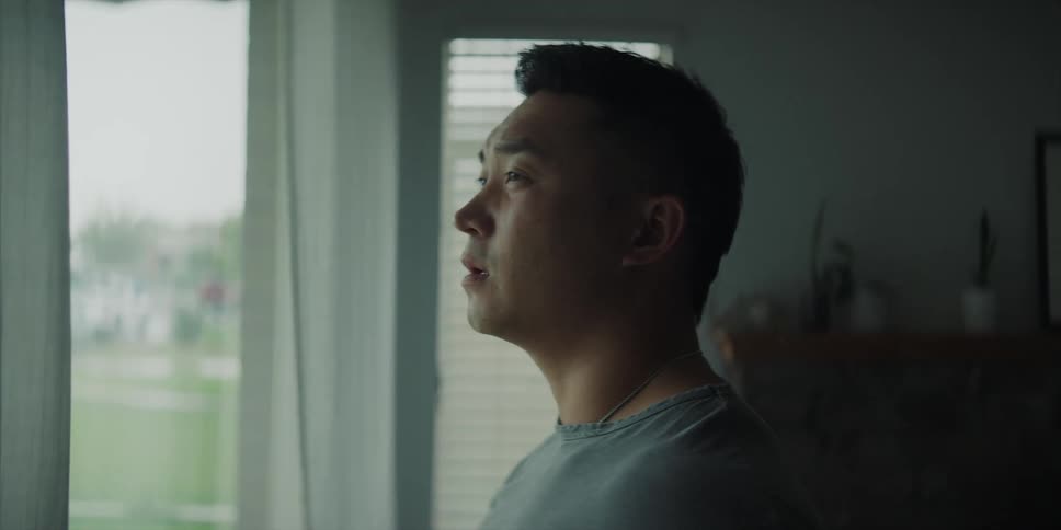A man drinks coffee from a mug while standing in his home looking out the window