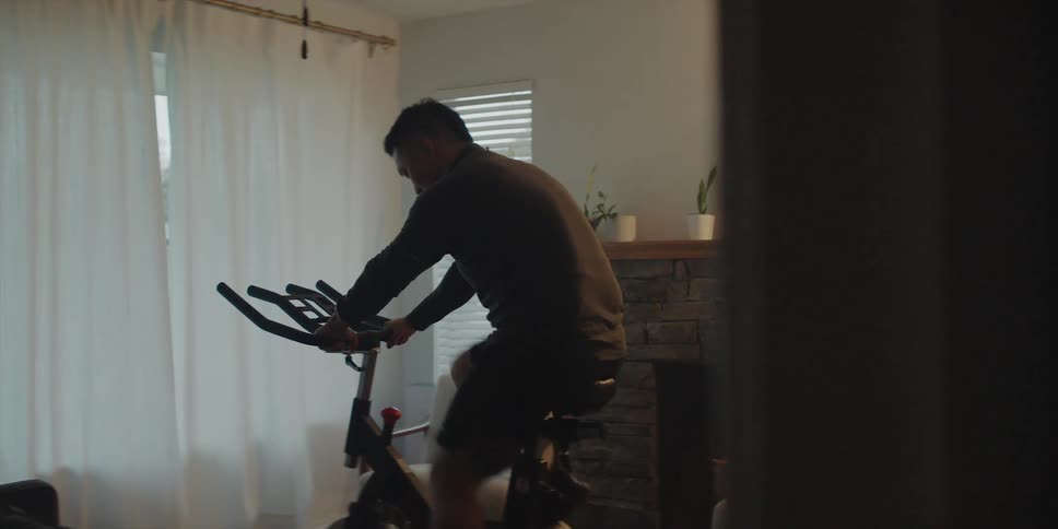 A man working out on his exercise bike in the living room facing the large window