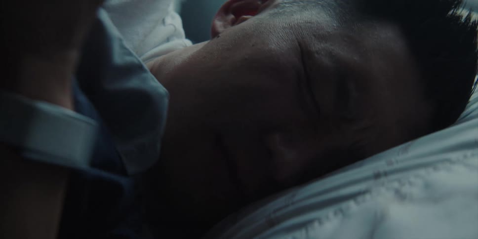 A man grimaces as if in pain as he turns and tries to get comfortable in bed
