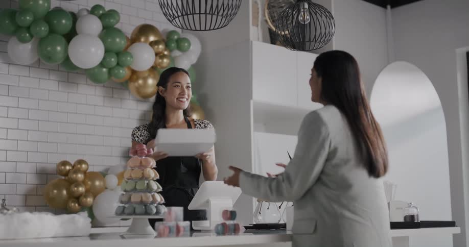 A bakery employee smiles and talks as she hands a box to a customer
