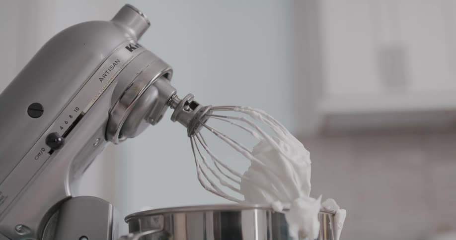 Freshly whipped cream clings to a whisk on a stand mixer