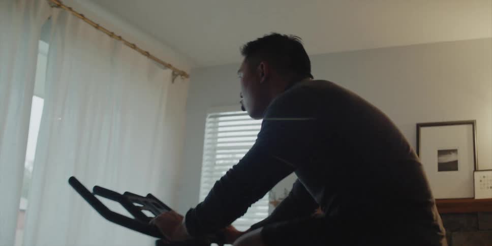 Man with shirt and shorts rides exercise bike in living room at home