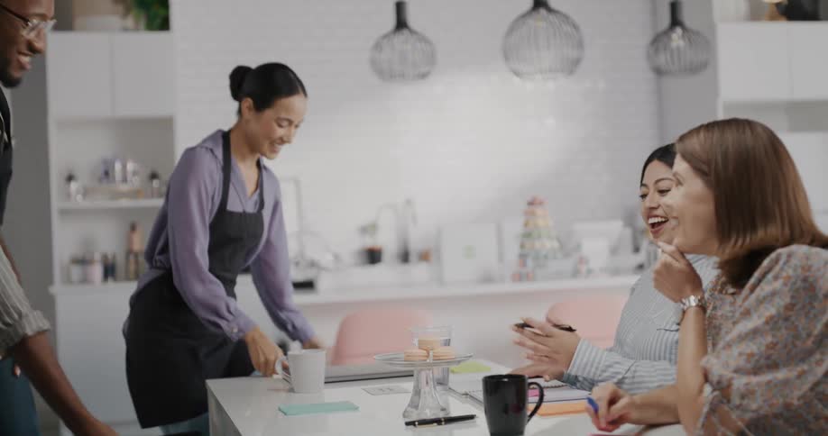 Two bakers join others at a table for a business meeting one with a laptop and the other with macaroons