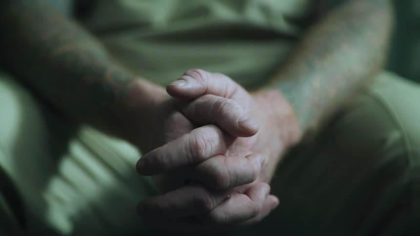 Close up of a man sitting with his hands clasped together