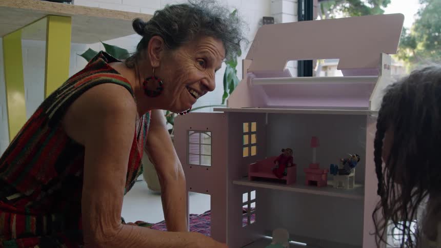 A grandmother is talking with her granddaughter by the doll house