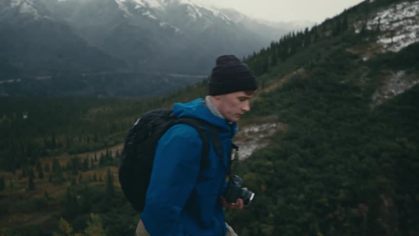 Male photographer with black beanie backpack and blue jacket hikes on the high mountain