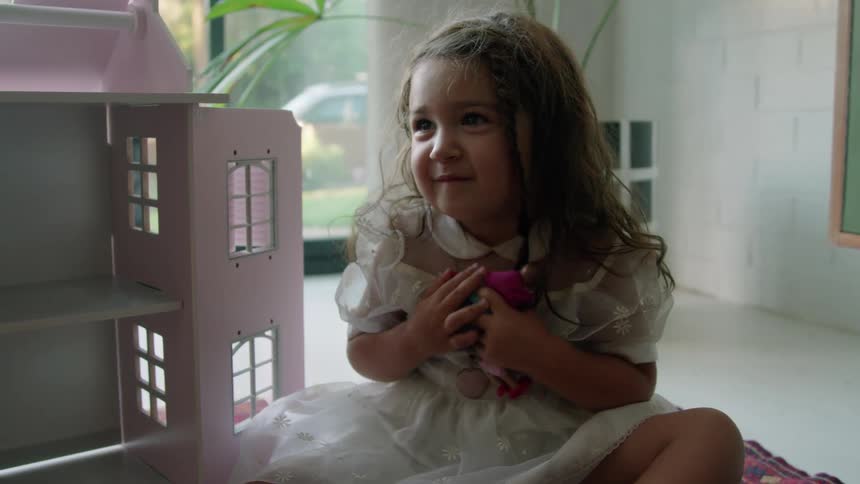 A little girl hugs her dolls to her chest as she plays in a house with her grandmother
