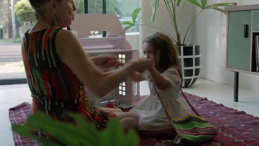 A woman holding a little girls hands moving them up and down making her laugh
