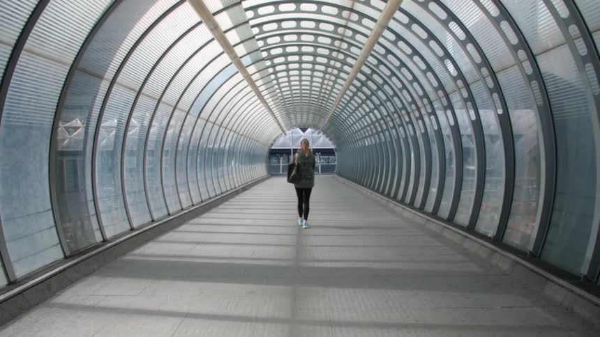 A woman walks through a glass tunnel with metal beams