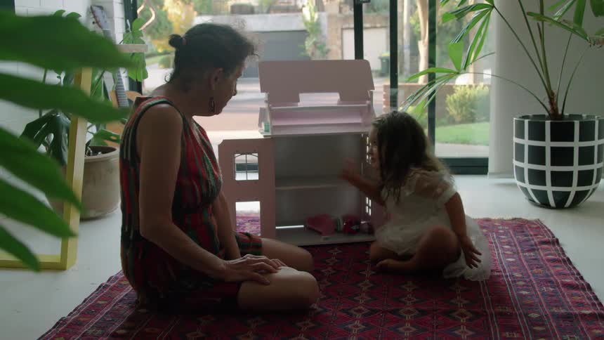 A grandmother talks to her granddaughter by the doll house