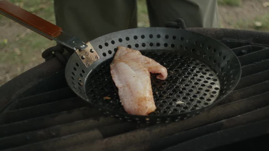 A person is outdoors grilling meat during the day time