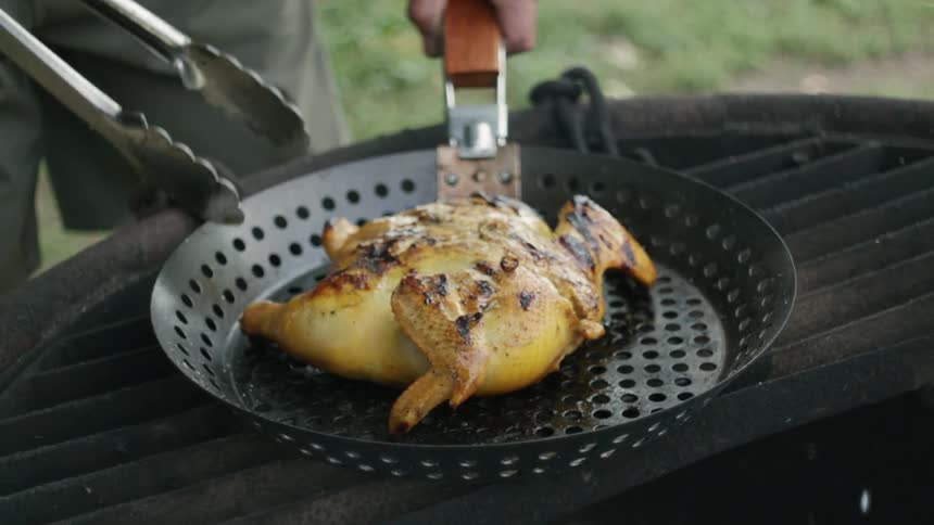 A man is cooking a whole chicken on a grill