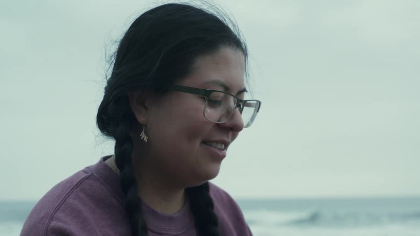 Woman with glasses and french braids uses smartphone on the beach smiling