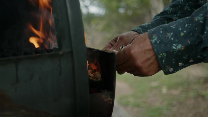 A person puts wood in the outdoor grill