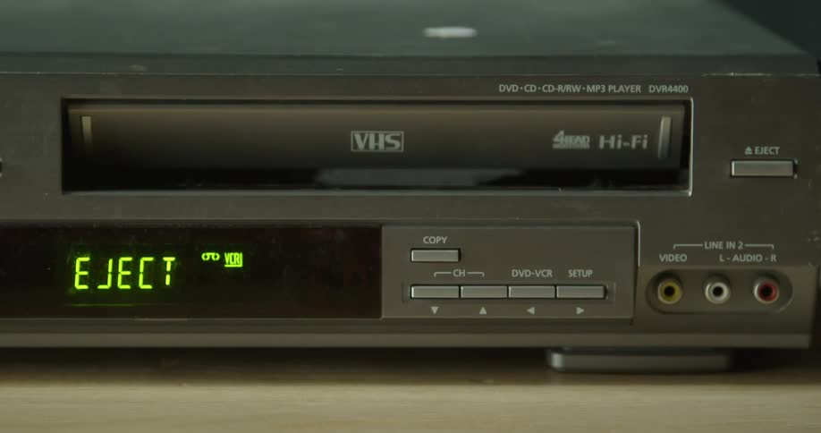 A person ejects the vhs tape from the player