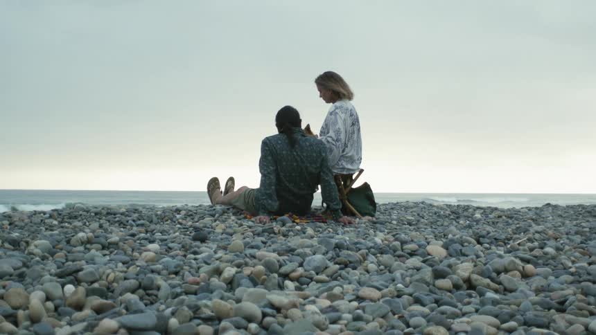 Man and woman sitting on pebble beach talk to each other