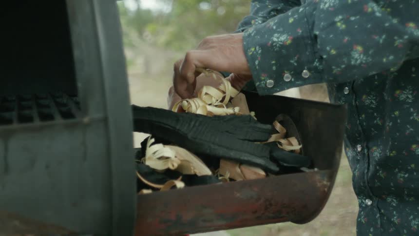 A man lights kindling on fire then places it in a grill