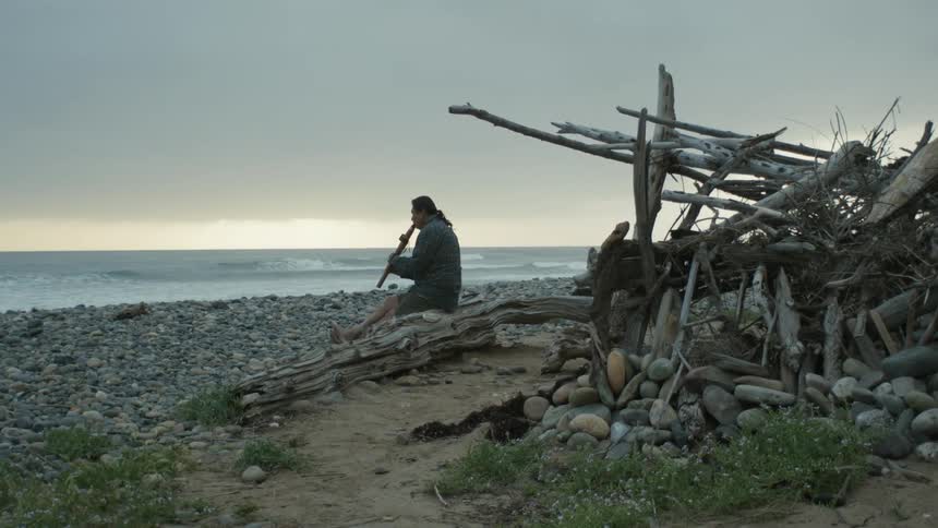 A man is sitting at the beach and playing an instrument