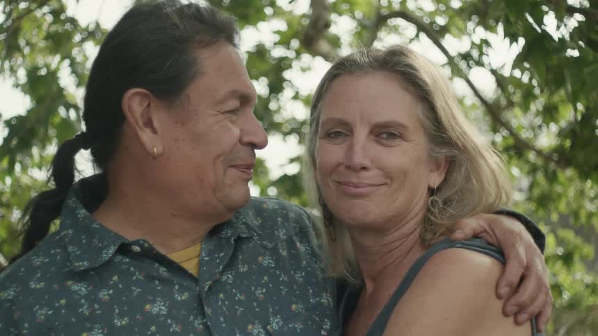 Middle aged couple cuddling and looking at each other in front of a tree outdoors