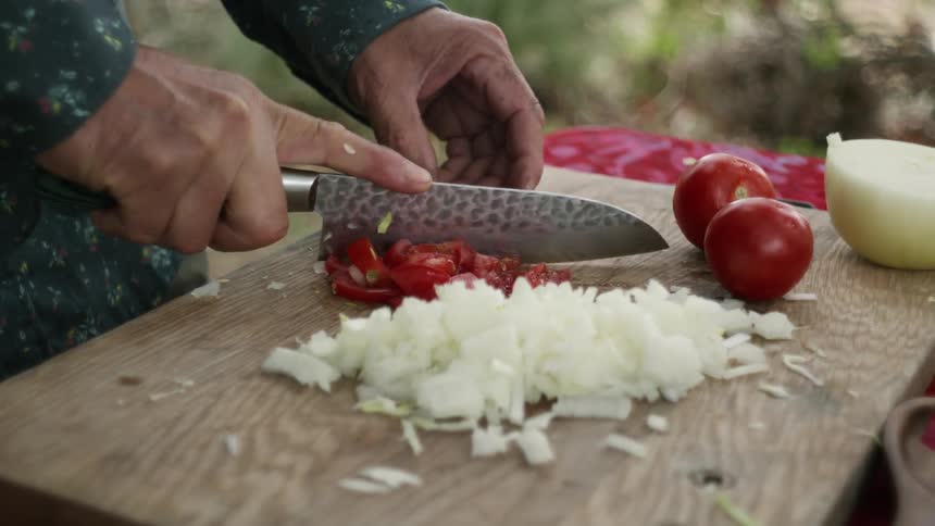 Man with blue hsirt cuts tomatoes and onions on cutting board outdoors