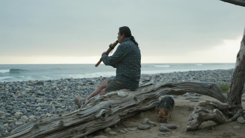 A man is playing an instrument while sitting at the beach