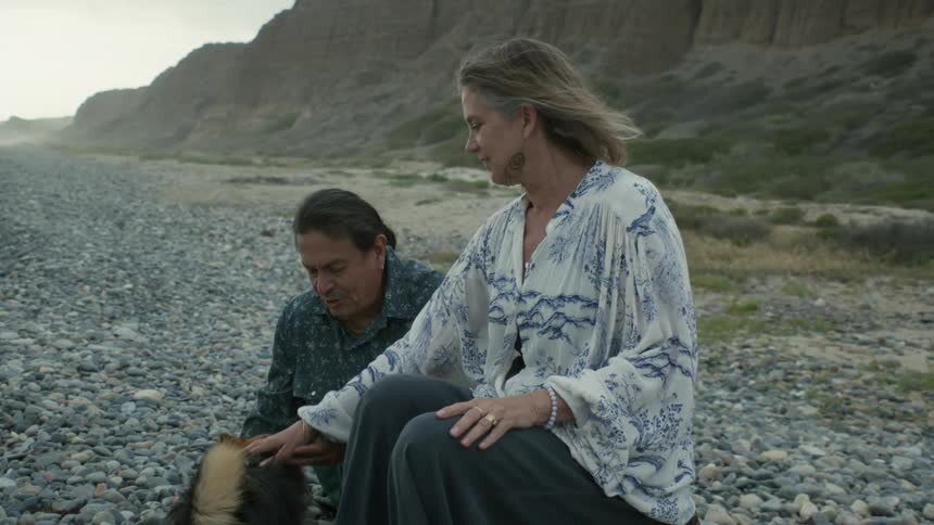 Man and woman are sitting outdoors with their pet dog