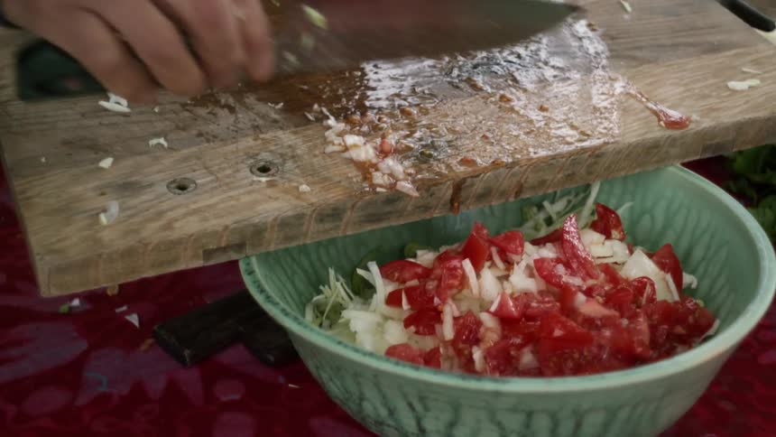 Man with blue shirt cuts onions and tomatoes and puts them in green bowl
