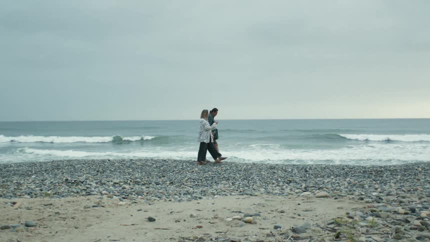 Couple walking together along the shoreline on an empty beach