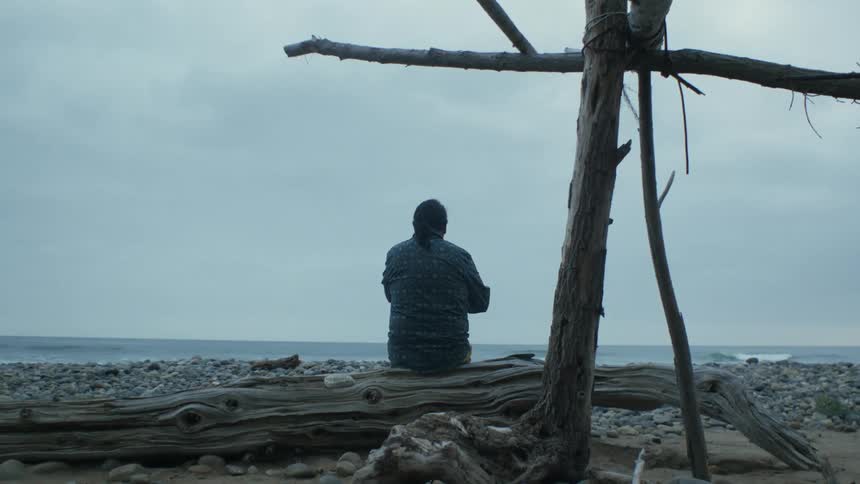 A man is sitting by the ocean and looking at the horizon