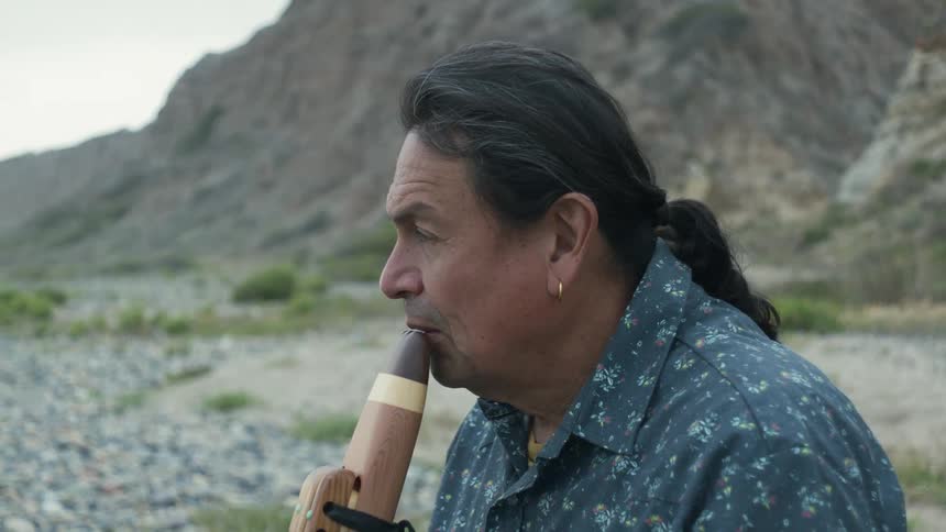 A man is playing an instrument and sitting outdoors