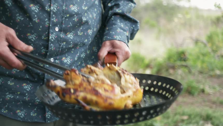 A man is grilling chicken outdoors in the wilderness
