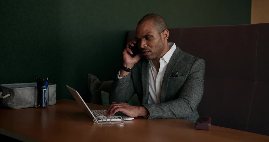 A man talks on his cell phone while typing on his laptop