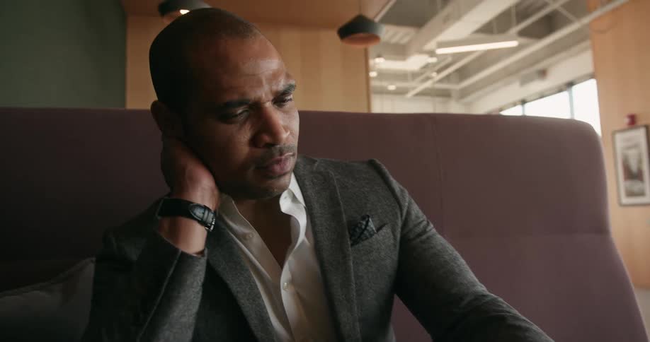 A man sits at a booth in a restaurant and rubs his neck as he looks at a tablet