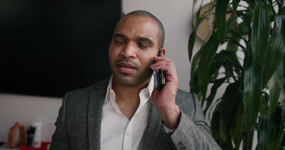 A man in an office talks on his cell phone as he looks at his watch