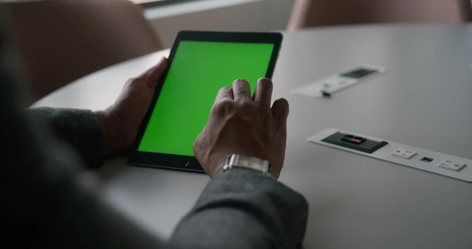 A man sits in an office and looks at a table with a green screen