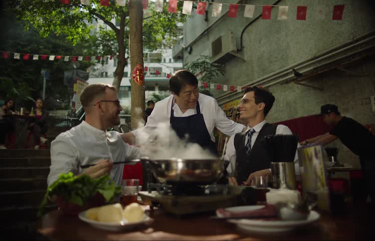 A waiter delivers vegetables for the hotpot and greets his smiling customers dining outside