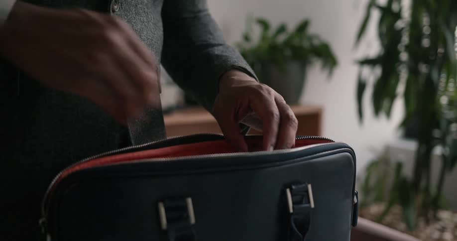 Man standing in his office opening up his suitcase and grabbing his laptop