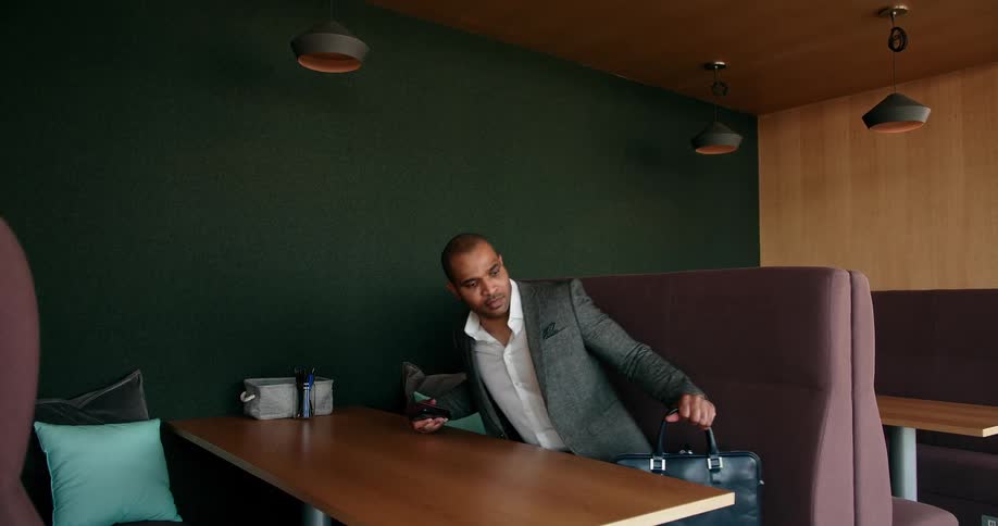 Man with gray blazer jacket and white shirt gets up from table in restaurant