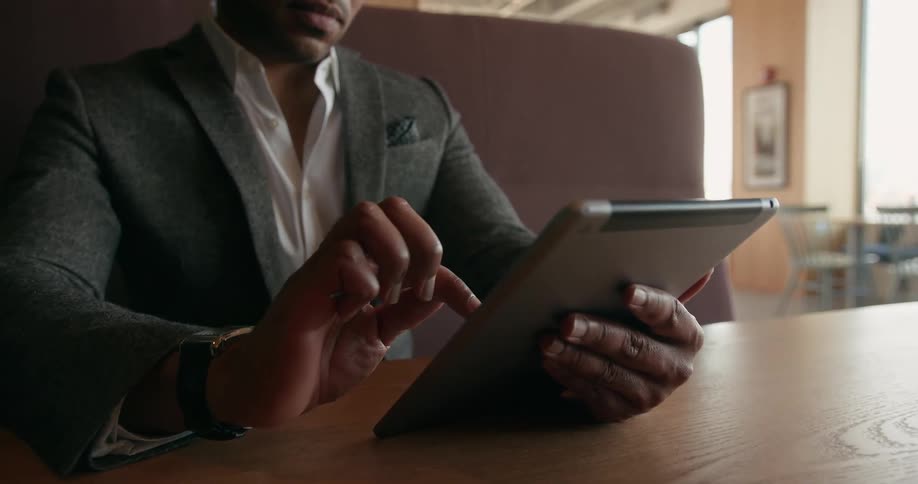 A man is sitting at a booth and browsing on his tablet