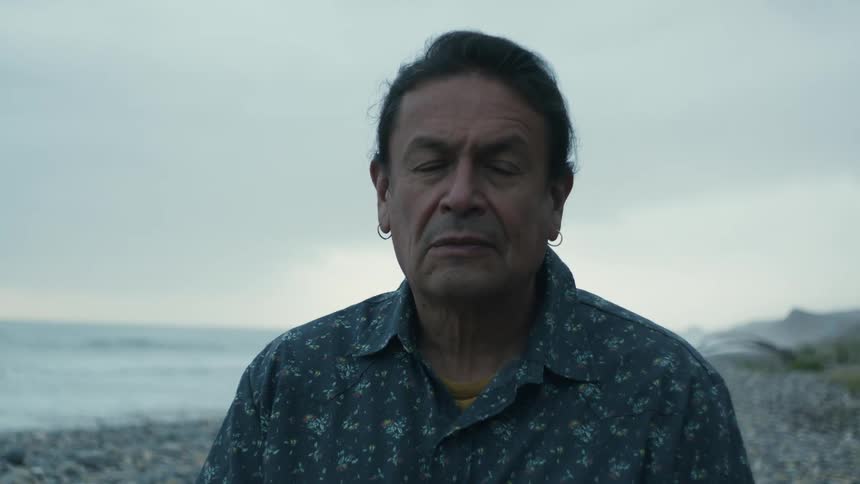 A man is playing an instrument and standing at the beach