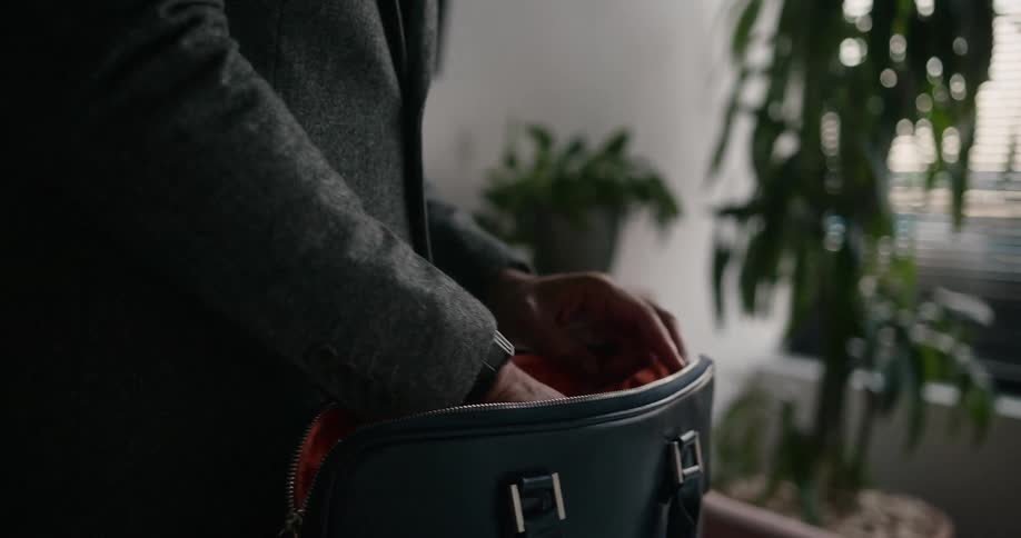 Man with gray blazer jacket takes laptop out of black briefcase in room
