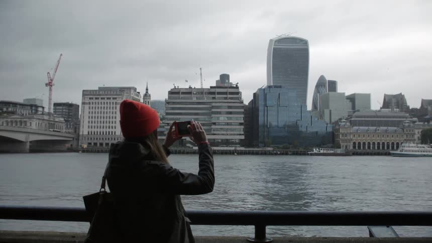 A woman photographs a city across the water
