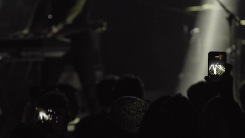 People in a crowd film a band performing onstage with their cellphones